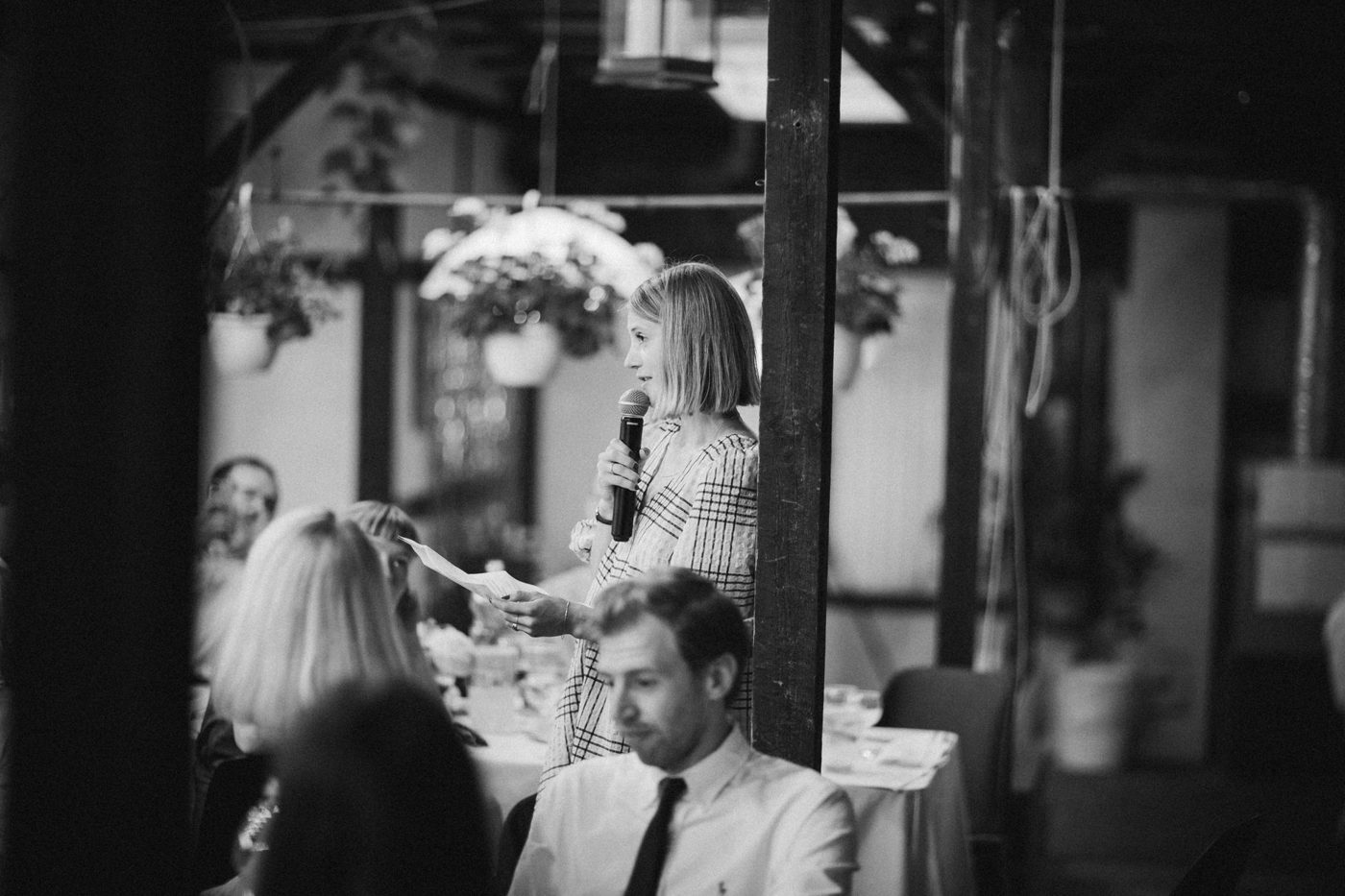 Father of the bride speaking to guests with a microphone and a glass in hand at a wedding reception