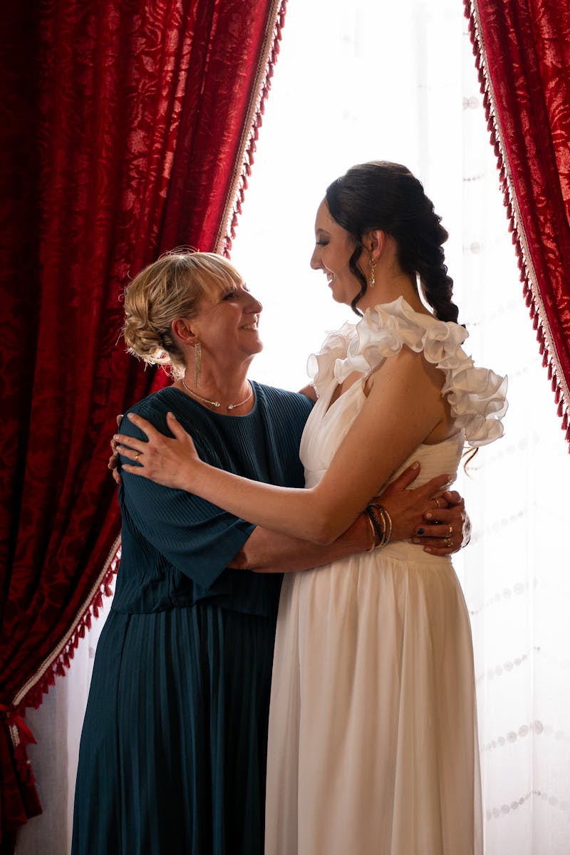 Mother of the bride holding her daughter's hands and smiling at the wedding reception
