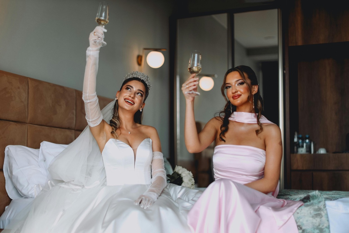 Bride and bridesmaid toasting with champagne glasses indoors
