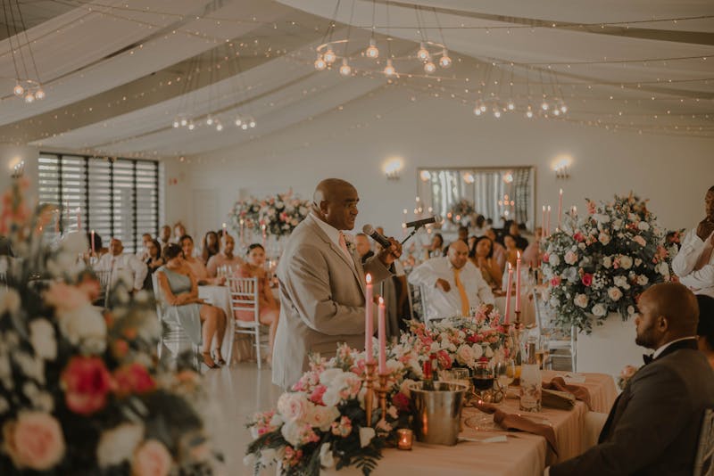 Couple smiling as guests raise champagne glasses during wedding toast