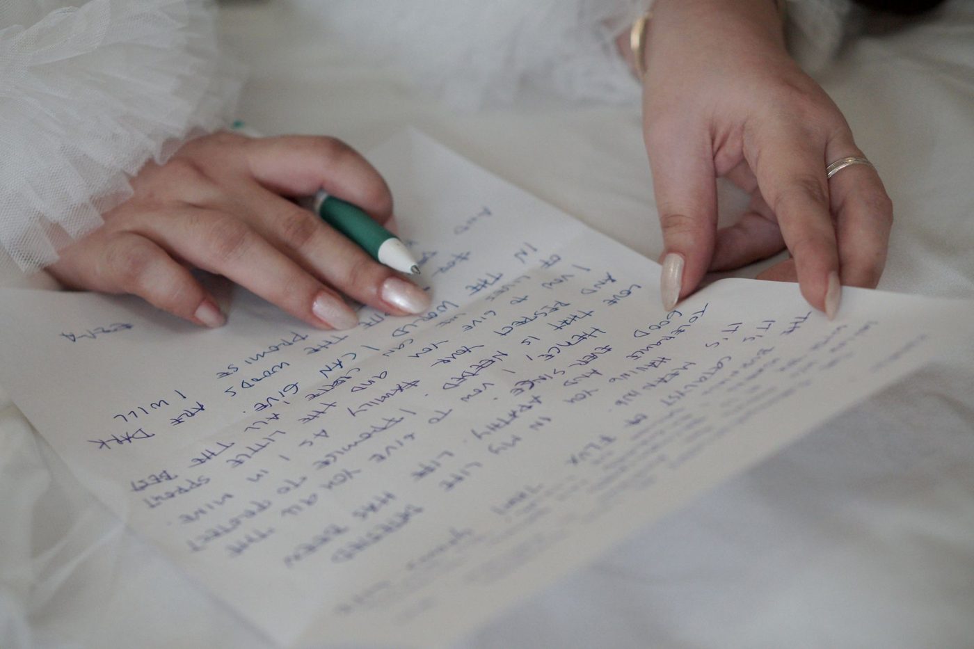 Hands writing wedding vows by hand on notebook paper with a green pen