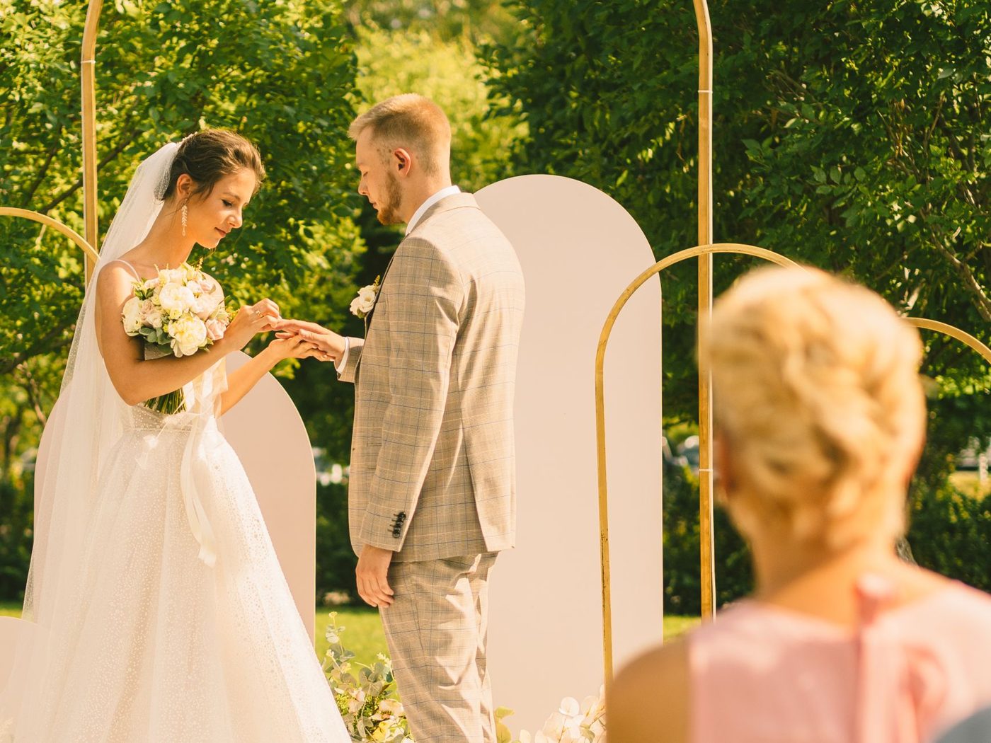 Groom holding a vow card and speaking to his bride during an outdoor wedding ceremony